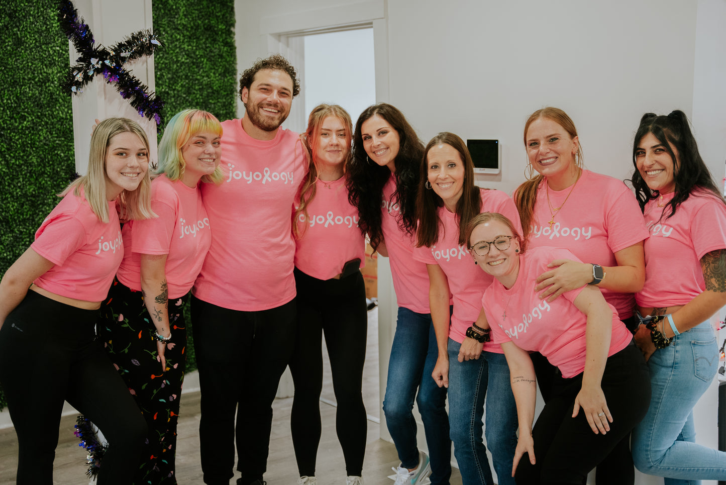 1 male and 8 females in group photo wearing pink Joyology breast cancer t shirts